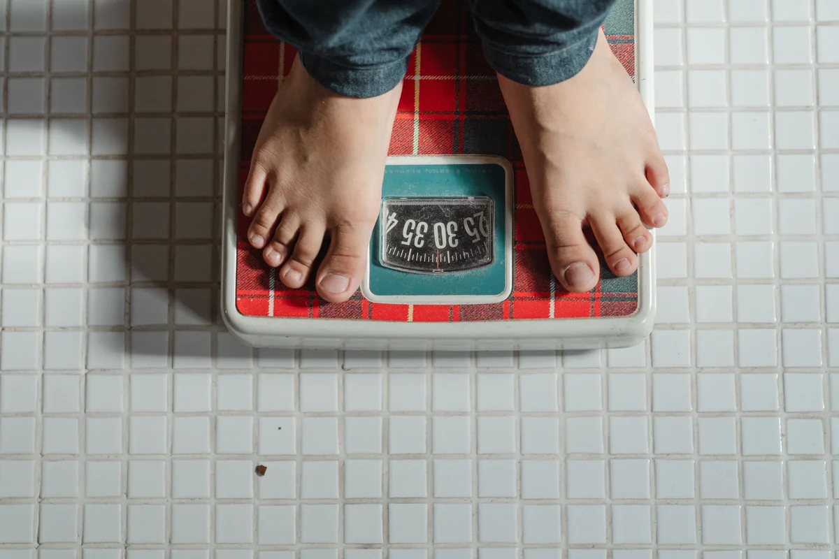 A barefoot child standing on a retro red and green analog bathroom scale, close to the age kids first ask what 40 kg means