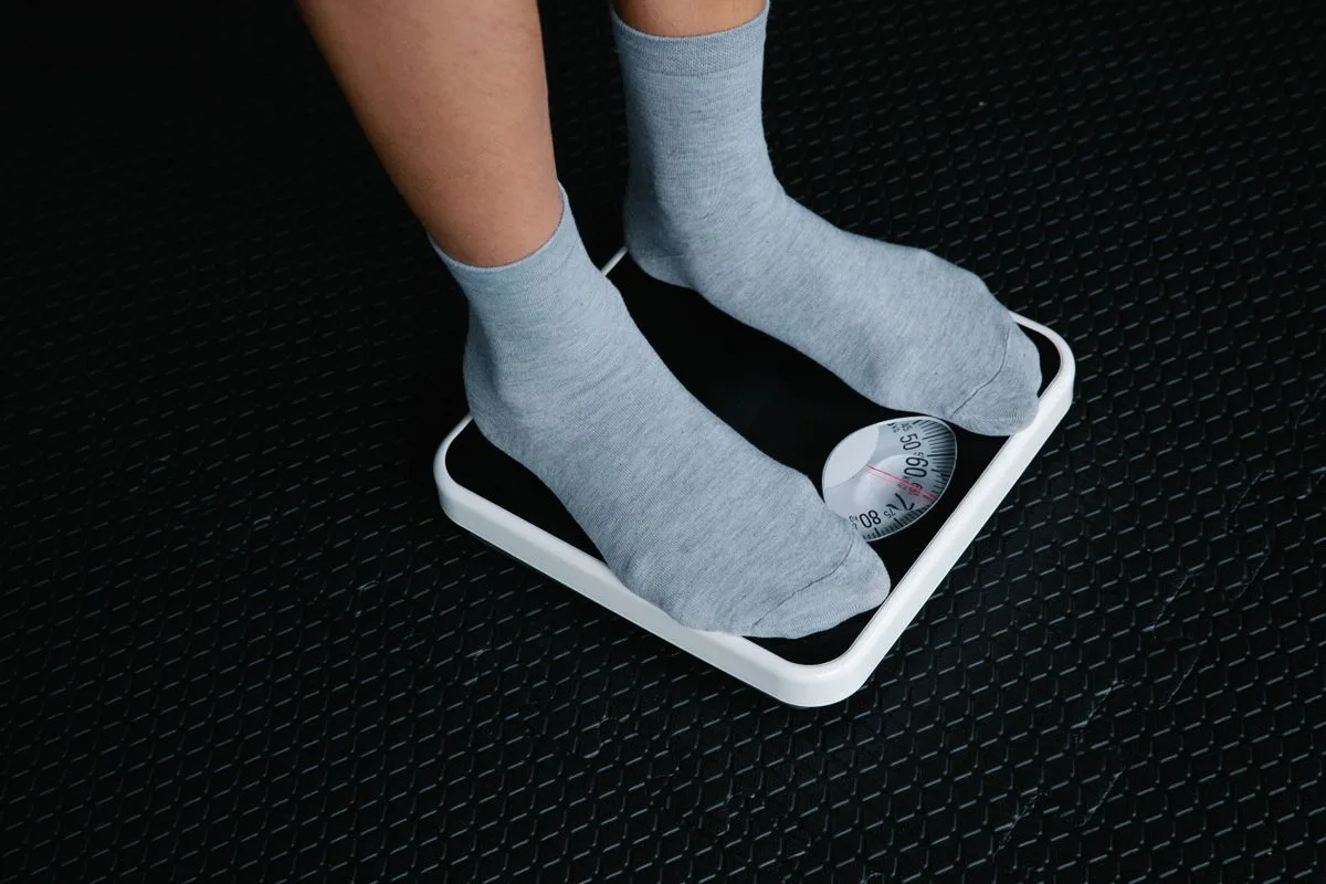 Feet in socks on a bathroom scale with the needle settling, the everyday way to check 75 kg